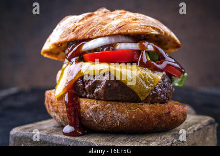 Barbecue Wagyu cheeseburger con cipolle e pomodori come close-up su un tagliere Foto Stock