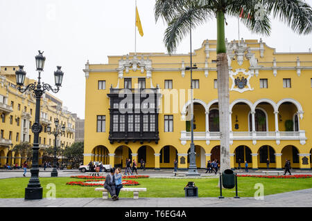 Un locale giovane seduta su una panchina con il palazzo comunale in background in Plaza de Armas o Piazza Principale nel quartiere storico di Lima, Perù Foto Stock