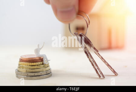 Le chiavi di casa in miniatura. Immobiliare di concetto. Mano azienda chiavi alla statuetta in miniatura seduti sulle monete, isolati su sfondo bianco Foto Stock