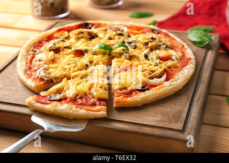 Scheda e la pala con una gustosa pizza sul tavolo di legno Foto Stock