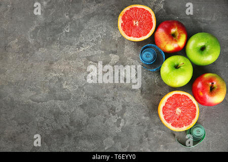 Frutti e nastri di misurazione su sfondo grigio. Cucina dietetica Foto Stock