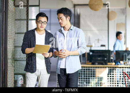 Due giovani colleghi asiatici discutere di affari mentre si cammina in ufficio.
