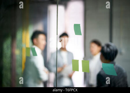 Giovani imprenditori asiatici di piccola impresa a discutere di business plan in office sala riunioni, concentrarsi sulle note di adesivo sul vetro. Foto Stock