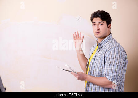 Giovane uomo applicando intonaco sulla parete di casa Foto Stock