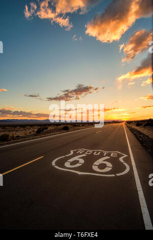 L'ampia strada aperta di route 66 che conduce verso un drammatico tramonti oltre l'orizzonte del Mojave Dessert appena fuori di Amboy, California. Foto Stock
