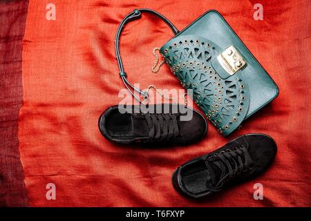 Alla moda in camoscio nero sneakers e un turchese borsa con motivi scolpiti e prigionieri di metallo su un tessuto rosso sfondo Foto Stock