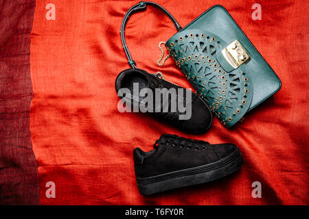 Alla moda in camoscio nero sneakers e un turchese borsa con motivi scolpiti e prigionieri di metallo su un tessuto rosso sfondo Foto Stock