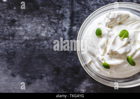 Cagliata cremosa crema di yogurt con menta in una ciotola su una retrò scuro dello sfondo. Vista superiore Foto Stock