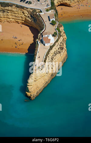 VISTA AEREA. Piccola cappella su un promontorio roccioso incredibilmente alto e stretto. Forte di Nossa Senhora da Rocha, Lagoa, Algarve, Portogallo. Foto Stock