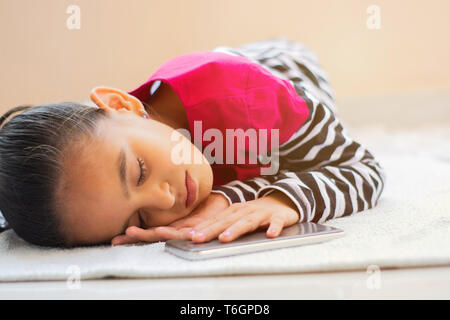 Carino little indian girl kid si addormentò con telefono cellulare accanto a lei sul letto. Foto Stock