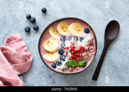 Acai frullato vegano tazza di cocco e rabboccato con banana, mirtillo, goji bacche e i semi di lino. Tabella vista dall'alto. Cibo crudo Foto Stock