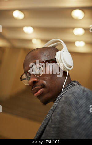 Testa e spalle ritratto di bello uomo africano che indossano le cuffie guardando la fotocamera mentre si ascolta la musica Foto Stock