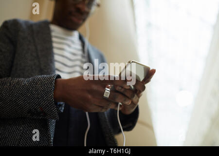 La sezione centrale verticale della moda uomo africano che indossano le cuffie utilizzando lo smartphone nel edificio di interesse architettonico, spazio di copia Foto Stock