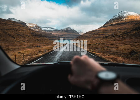 Autista della prospettiva dall'interno di un auto durante un viaggio su strada attraverso valli imbiancate sulle Isole Faerøer con vedute panoramiche (Isole Faerøer) Foto Stock