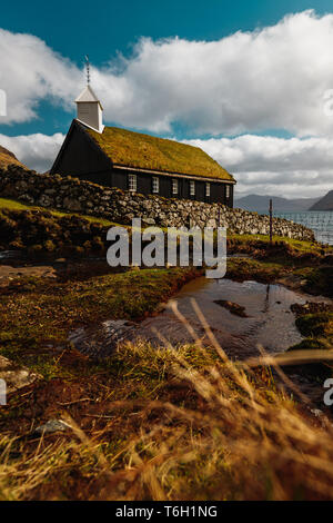 Il piccolo e pittoresco di legno nero chiesa di Funningur (Funnings Kirkja) durante una soleggiata giornata di primavera con drammatica nuvole (Isole Faerøer, Danimarca) Foto Stock