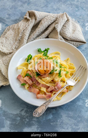 La pasta alla carbonara con tuorlo d'uovo in una piastra bianca. Foto Stock