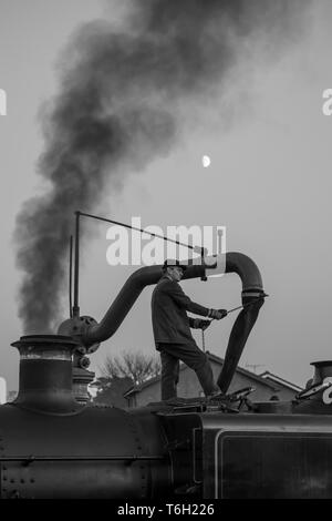 Bianco & Nero colpo di locomotiva a vapore membro di equipaggio isolato permanente sulla sommità di vintage UK motore a vapore usando acqua gru e il riempimento di un serbatoio dell'acqua. Foto Stock