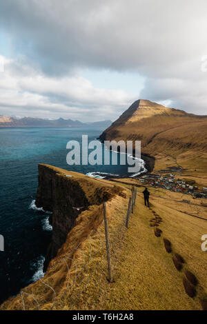 Un escursionista solitario su un trekking panoramico con vedute spettacolari di Gjógv e dalle montagne circostanti e sul mare (Isole Faerøer, Danimarca, Europa) Foto Stock