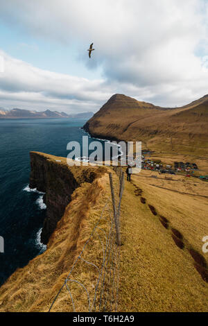 Un escursionista solitario su un trekking panoramico con vedute spettacolari di Gjógv e dalle montagne circostanti e sul mare (Isole Faerøer, Danimarca, Europa) Foto Stock