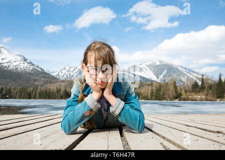 Giovane ragazza è giacente su tavole di legno in montagna vicino al lago - premuroso gesto Foto Stock