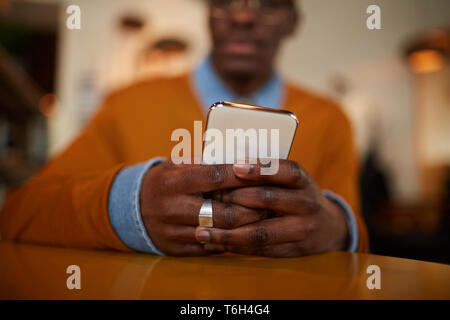 Close up africana contemporanea uomo utilizza lo smartphone seduta a tavola in cafe, spazio di copia Foto Stock