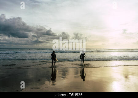 Drammatica foto di due surfers inserendo l'oceano con le loro tavole da surf Foto Stock