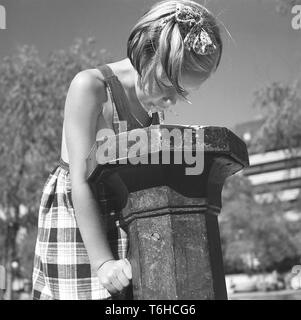 Estate di 1940s. Una giovane ragazza in un abito di estate bevande da una fontana di acqua in uno dei parchi di Stoccolma. Queste fontane pubbliche erano comuni e in questo momento è azionato spingendo la leva verso il basso e che l'acqua ha iniziato a flusso. La Svezia Luglio 1940 Kristoffersson foto Foto Stock