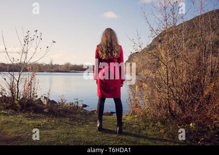 Giovane donna guarda oltre Duddingston Loch in Edinburgh Foto Stock