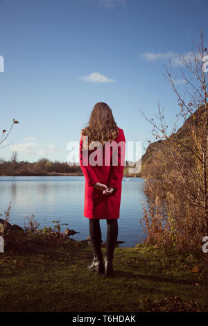Giovane donna guarda oltre Duddingston Loch in Edinburgh Foto Stock