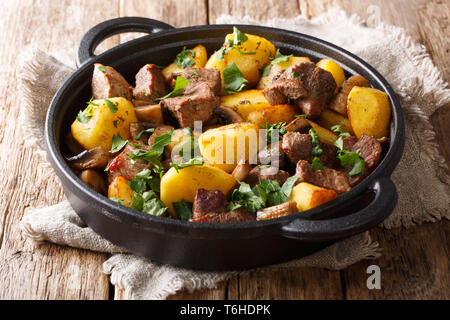 Semplice pasto abbondante di patate fritte con carne di maiale e funghi close-up in una padella sul tavolo orizzontale. Foto Stock