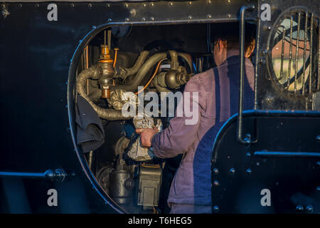 Vista posteriore ravvicinata, conducente del treno a vapore isolato nella cabina del motore sulla pedana della locomotiva a vapore vintage del Regno Unito, al controllo della prima sera. Treni a vapore nel Regno Unito. Foto Stock