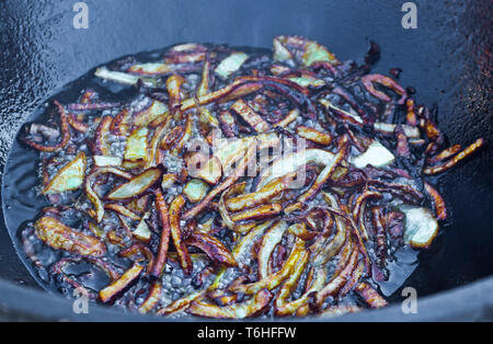 Le cipolle sono fritte in olio bollente in un paiolo di rame per pilaf Foto Stock