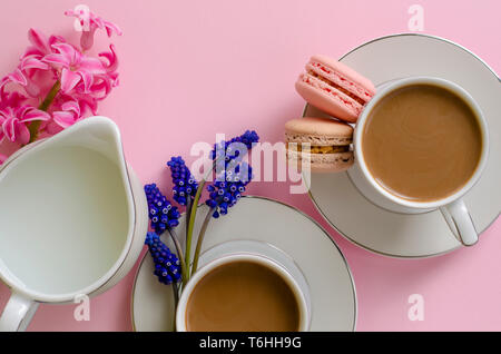 Tazza di caffè con latte, amaretti, latte jar pastello su sfondo rosa decorata con muscari e fiori di giacinto. Vista superiore, piatto laici. Morni romantica Foto Stock