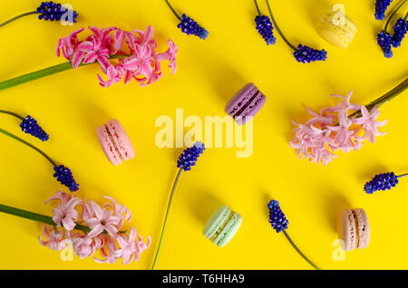 Muscari azzurro fiori rosa, giacinto e macarons o amaretti su sfondo giallo. Nessuna dieta giorno. Piatto, laici vista superiore Foto Stock