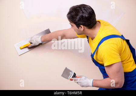 Giovane dipendente del contraente di applicare gesso sulla parete Foto Stock