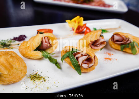 Spuma di Formaggio con bacon in eclair, servita su un piatto e ricoperta di verde e pomodoro cherry Foto Stock