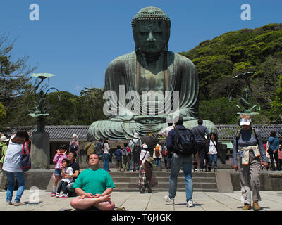 Turist meditando nella posizione del loto sotto il Grande Buddha (Daibutsu) adducendo il motivo del tempio Kotokuin a Kamakura, Giappone. Foto Stock