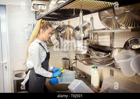 Lo chef del ristorante piccolo lavaggio piatti nel lavandino alla fine della giornata di lavoro - cucina lavoratore utilizzando una spugna per pulire i piatti - una giovane donna al lavoro in eatery Foto Stock