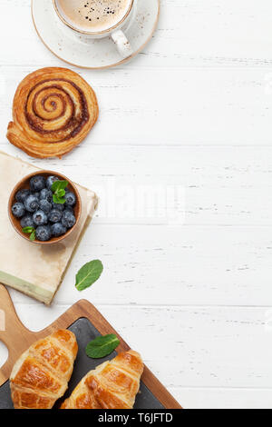 Caffè, cornetti, panini alla cannella e le bacche di prima colazione. Su un tavolo di legno. Vista da sopra con copia spazio per il testo Foto Stock