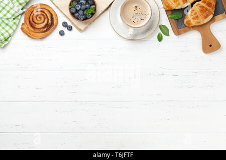 Caffè, cornetti, panini alla cannella e le bacche di prima colazione. Su un tavolo di legno. Vista da sopra con copia spazio per il testo Foto Stock