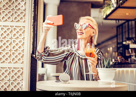 Sorridente donna bionda che indossa gioielli lunga e occhiali da sole rosso Foto Stock