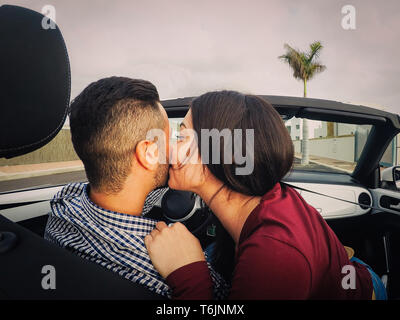 Coppia giovane kiss in una vettura convertibile durante il loro viaggio su strada - Happy romantico sposa data alla guida di una cabriolet auto in luna di miele Foto Stock