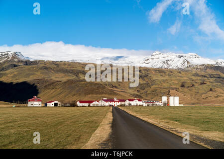 Vista di una strada che conduce a una fattoria ai piedi della coperta di neve vulcano Eyjafjallajökull. Il vulcano errupted notoriamente nel 2010. Foto Stock