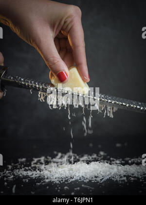La mano di una donna reticolo parmigiano su uno sfondo nero. Dark cibo. Formaggio Parmigiano Reggiano Foto Stock