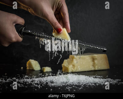 La mano di una donna reticolo parmigiano su uno sfondo nero. Dark cibo. Formaggio Parmigiano Reggiano Foto Stock