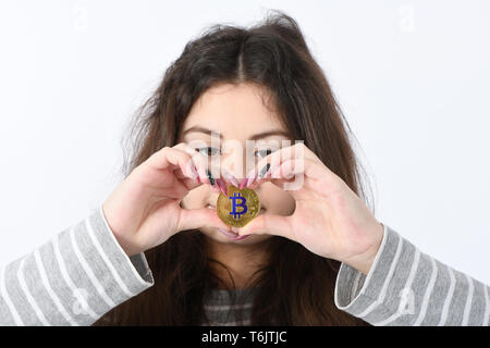 Pretty Girl holding e mostra il cuore nuovo golden cryptocurrency bitcoin in mani su sfondo bianco Foto Stock