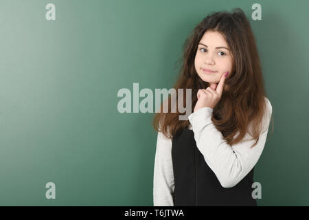 Sorridente Little Schoolgirl mostra sulla sua guancia sfondo verde Foto Stock