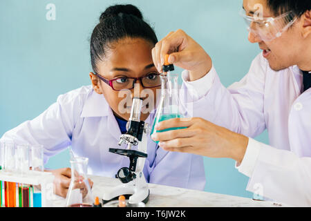 Maschio asiatici docente di scienza e di insegnamento di chimica facendo prova di laboratorio a curiose americano africano studente elementare - istruzione per i bambini concept Foto Stock