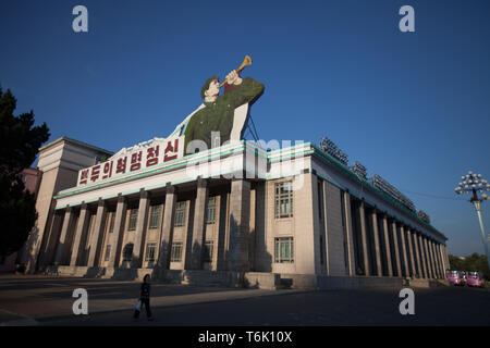 Un edificio ad angolo di Kim Il Sung Square a Pyongyang ha una grande immagine di un bugler del con i messaggi sul tetto. Foto Stock