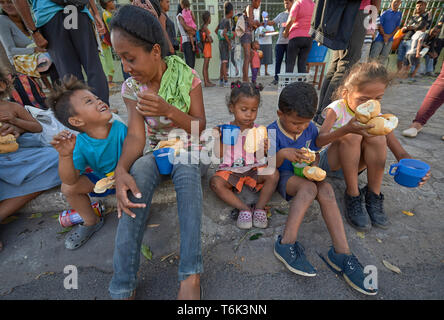 Rifugiati venezuelano di sedersi su un cordolo in Boa Vista, Brasile, mangiare la colazione fornita da Sorelle Missionarie della Consolata. Foto Stock